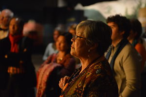 Woman stands in front of others listening to speaker.