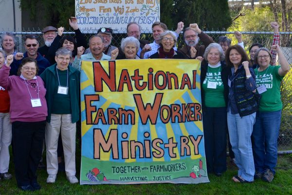 Many people stand with a sign that reads National Farm Worker Ministry: Together with Farmworkers Harvesting Justice. 