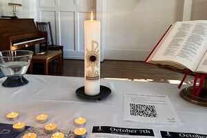 A candle on a table and bulletin that reads "October 7 Open Chapel"