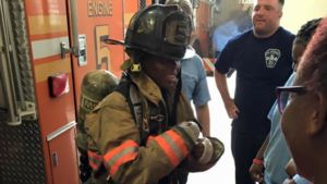 A child tries on firefighter gear in front of a fire truck at a a fire station.