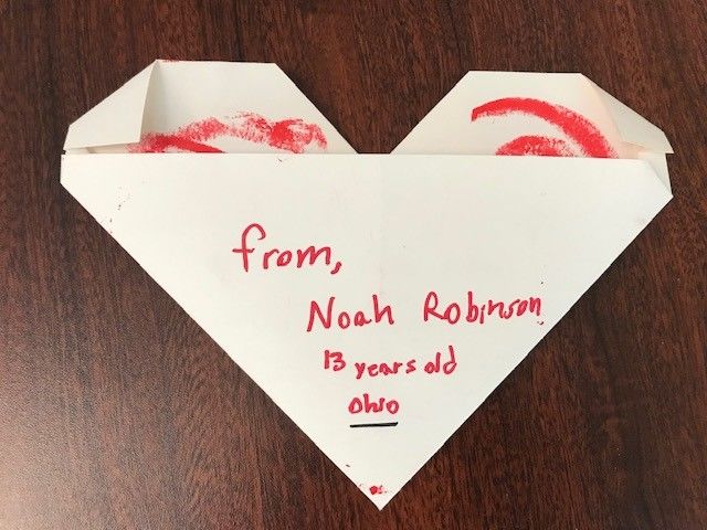 A letter folded in the shape of a heart sits on a table. The letter reads, "From, Noah Robinson, 13 years old. Ohio." 