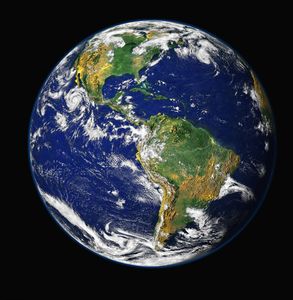 A full view of the earth from space. It centers on North and South America, with clouds swirling over them. The background is the black, mildly starry cosmos.