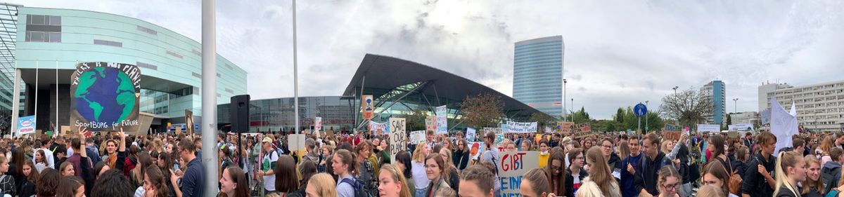 A panoramic shot of people protesting. One sign reads, "Save our planet." 