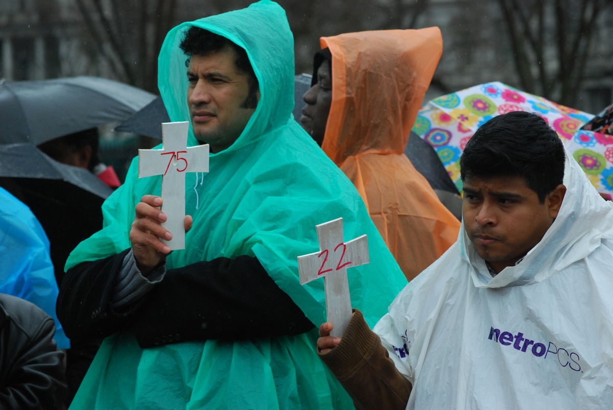 Two men hold crosses with numbers representing those killed in immigration raids