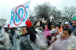 People protesting, a person holds up a sign that says "No More Raids"