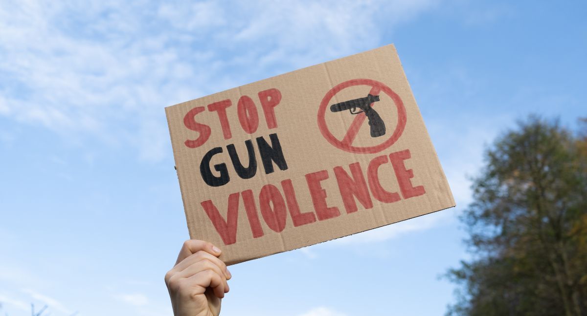 A hand holding up a sign that says "STOP GUN VIOLENCE"