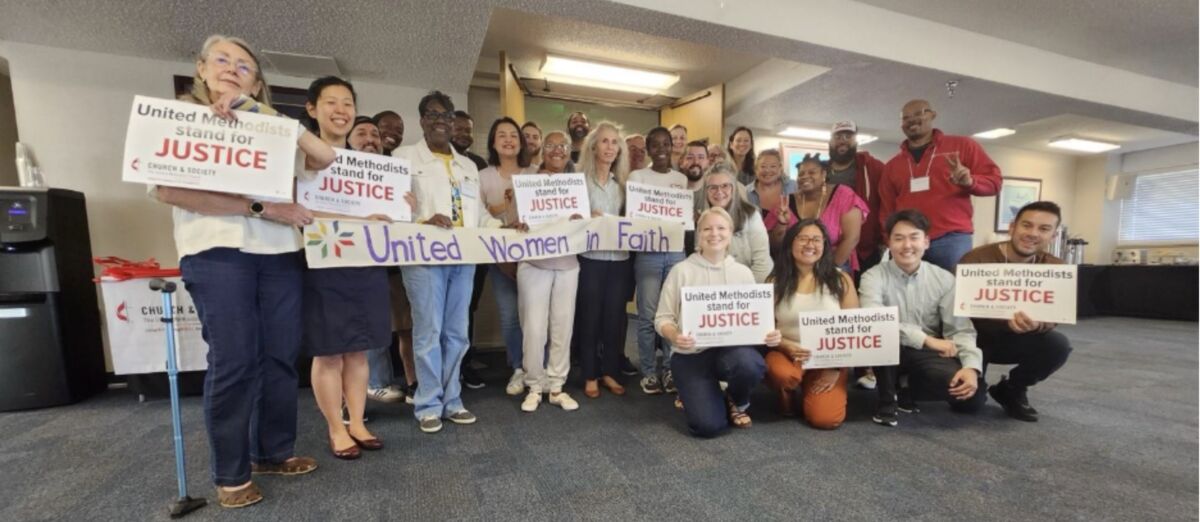 Grassroots organizing training group photo, with participants holding signs that read "United Methodists Stand for Justice" and a banner that reads "United Women in Faith"