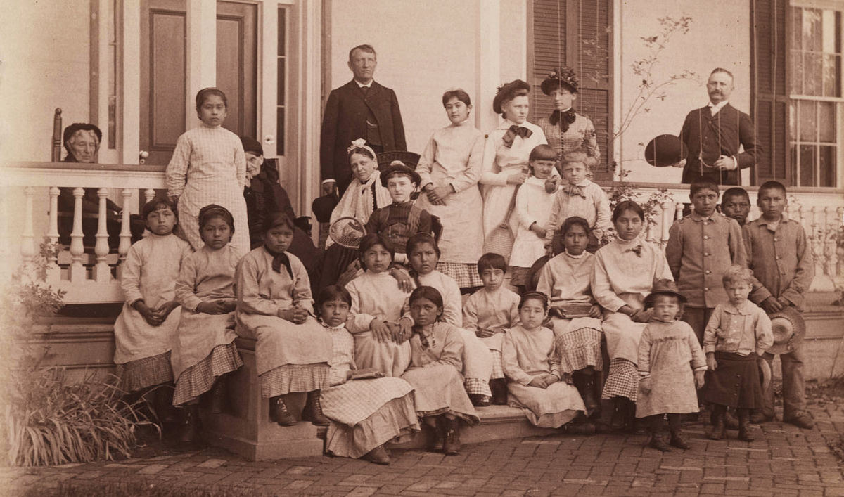 Photograph of Capt. Pratt and students at the Carlisle Industrial School, black and white photographic print, 13 cm x 21.5 cm. Capt. Richard Henry Pratt served as the head of the Carlisle Industrial School, where Native Americans were sent. Photograph circa 1900 (undated). Pratt died in 1924. Courtesy of the Yale Collection of Western Americana, Beinecke Rare Book and Manuscript Library, Yale University, New Haven, Connecticut. Public Domain via Wikimedia Commons.