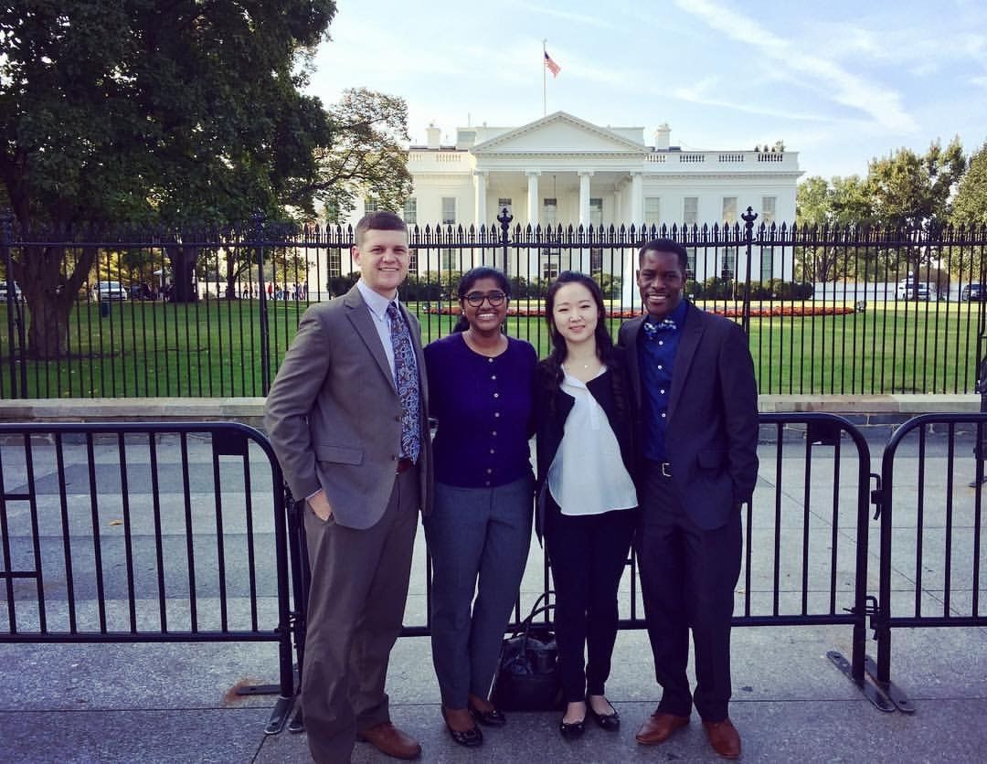 Four people stand in front of the White House.